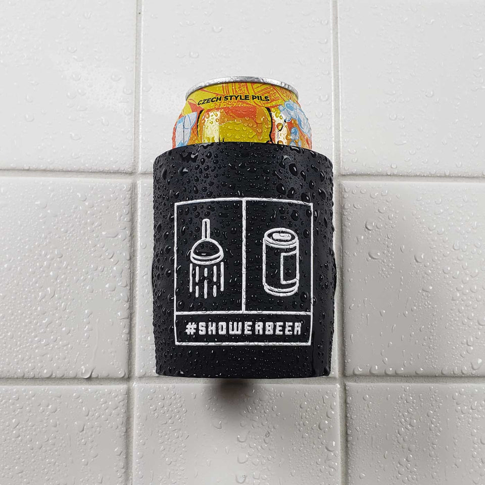 Foam can beverage holder that sticks to shower wall via industrial velcro. This design is white ink printed on a black can holder with the words "#SHOWERBEER" written across the bottom and the artwork depicting a shower head and a canned beer beverage. This is an action shot of the product in a shower.