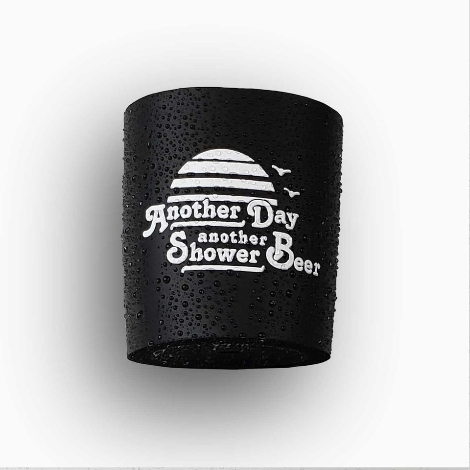 Foam can beverage holder that sticks to shower wall via industrial velcro. This design is white ink printed on a black can holder with the words "Another Day Another Shower Beer" written and artwork depicting a California sunset and two seagulls flying.