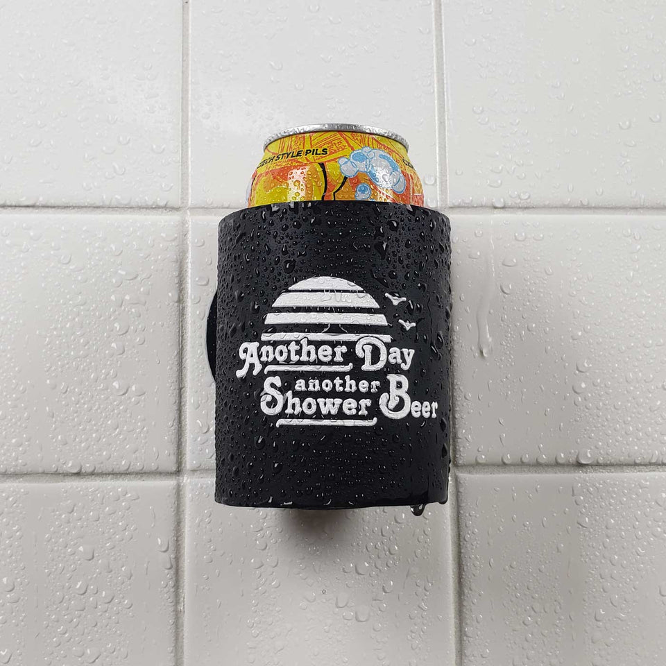 Foam can beverage holder that sticks to shower wall via industrial velcro. This design is white ink printed on a black can holder with the words "Another Day Another Shower Beer" written and artwork depicting a California sunset and two seagulls flying. This is an action shot of the product sticking to a shower wall.